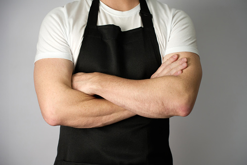Male chef arms crossed wears apron standing on white background, close-up