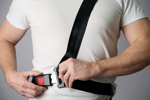 Close-up of a man hand fastening a seat belt. Man driver fastens his seat belt over white background. Driving safety concept.