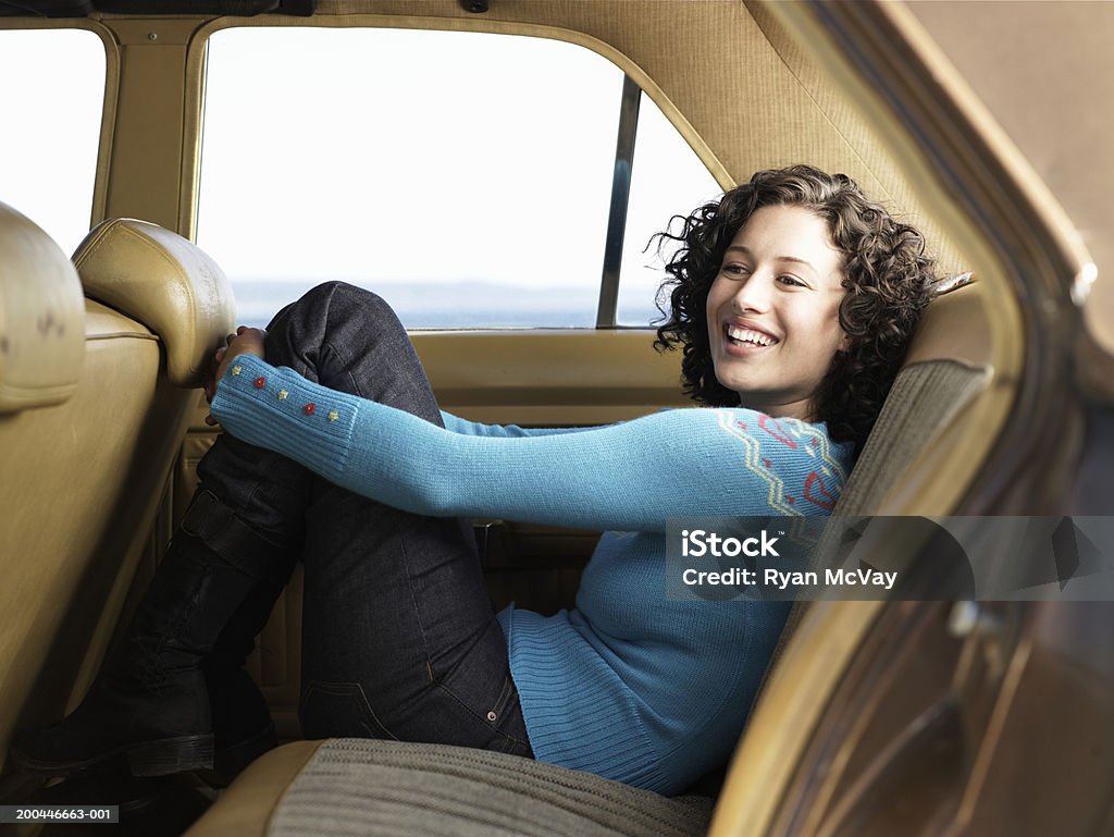 Young woman hugging knees in back seat of car, laughing, side view  Car Stock Photo