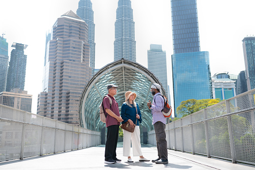 Two senior Asian tourist enjoy their city walking tour with a Sikh tour guide through the famous Saloma Bridge landmark in the city of Kuala Lumpur, Malaysia.