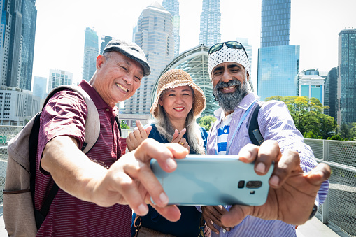 A senior Sikh tour guide and two senior Asian tourist taking selfie together in front the famous Saloma Bridge in the city of Kuala Lumpur.