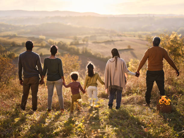 Back view of black extended family holding hands on a hill at sunset.