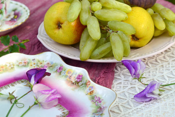 Fresh grains of white grapes and a petal of orange are placed in a golden patterned plate and they are placed on a white marble table.