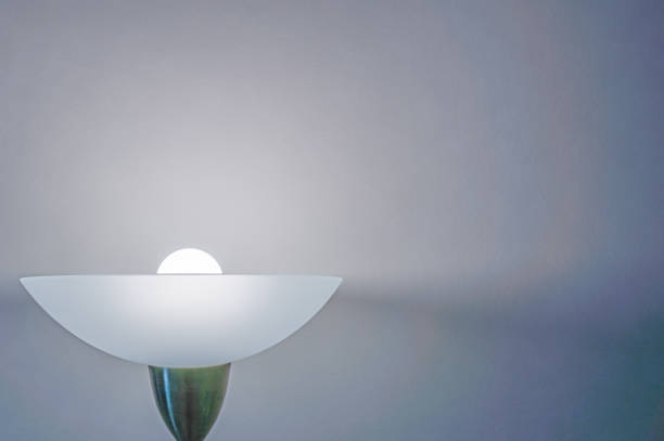 A floor lamp illuminates a white wall in the semi-darkness. Modern background with copy space.