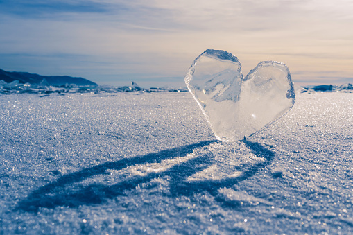 Arctic landscape with a transparent icy heart, frozen snow of Lake Baikal or extreme Antarctica. An icicle in the shape of a heart on ice. An icy heart. Selective focus. An icy heart in the sunset light. An icicle in the shape of a heart on the ice of the lake. Frozen. Love of nature. An Arctic landscape with a transparent ice heart, frozen snow of Lake Baikal or extreme Antarctica. Selective focus.