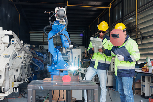 Two mechatronics engineers are beginning to test for welding a metal piece with a robotic arm