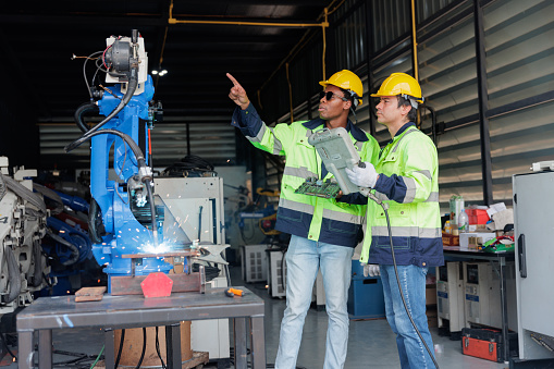 Two mechatronics engineers are beginning to test for welding a metal piece with a robotic arm