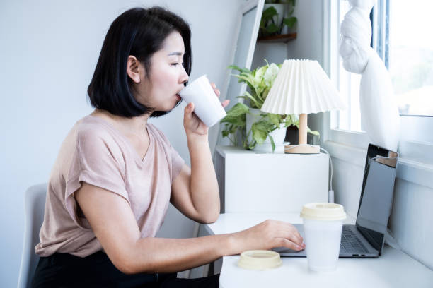 istock caffeine addiction concept with Asian woman drinking too much coffee while working on computer 2004577150