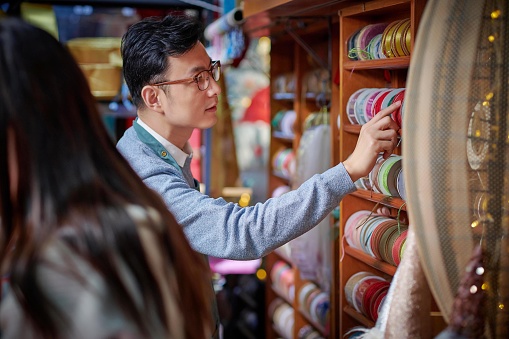 Asian male craftsperson choosing ribbons & females craftsperson wrapping gift box.