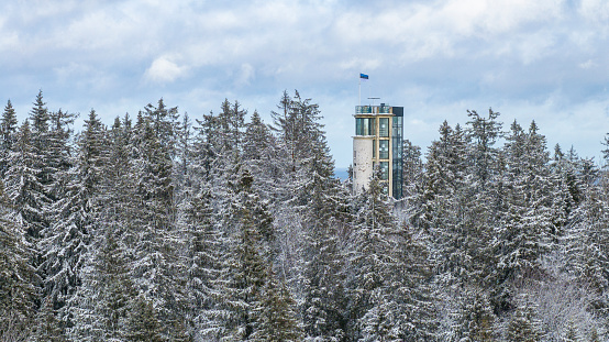 An aerial view of the wintertime snow-clad forested Suur-Munamagi hill with the watchtower and Estonian flag flying