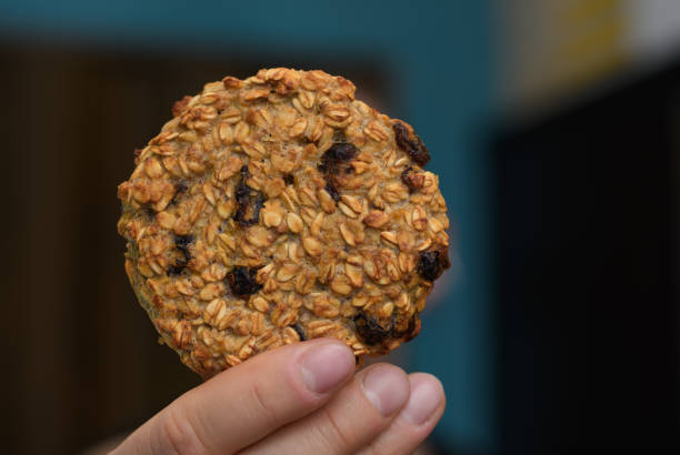 One single round oatmeal cookie held in hand, with raisins
