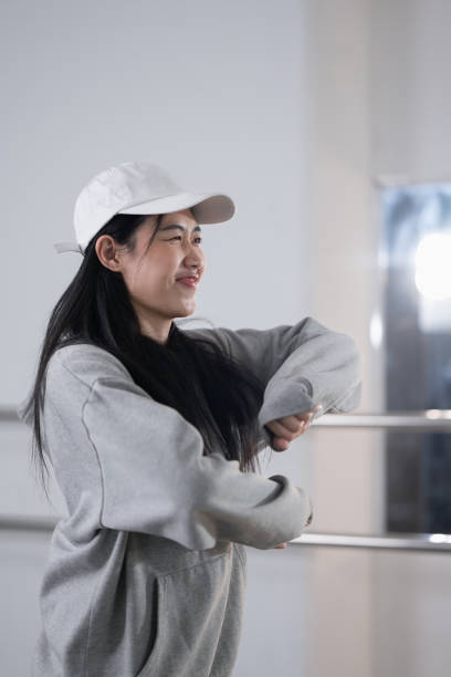 istock Pretty young woman in hoodie and cap enjoy practicing break dance at studio. 2004608378