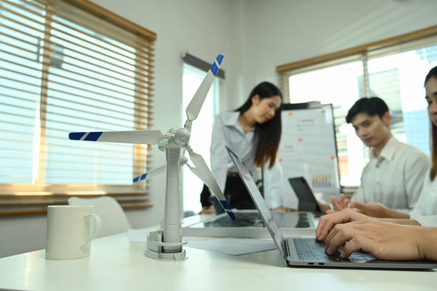 istock Wind turbine model on a meeting table with business people brainstorming project in background. 2004609442