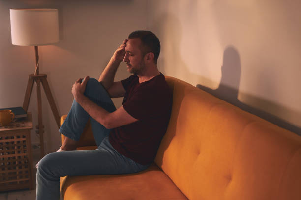 istock Man with headache and knee pain sitting on a sofa at home. 2004615312