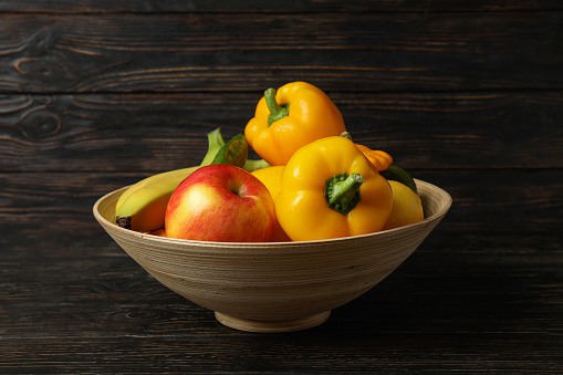 Bowl with vegetables and fruits on wooden background
