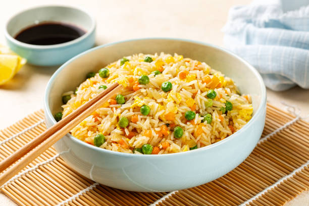 istock Bowl with Fried rice with egg and vegetables, onion, bell pepper, carrot, green peas, soy sauce on background. Prepared and served in a light blue plate. 2004659042