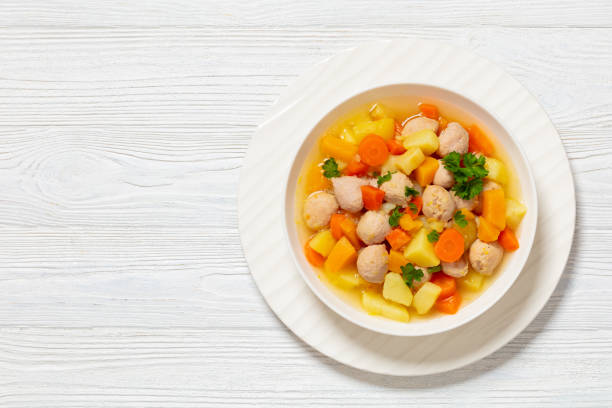 siskonmakkarakeitto, finnish sausage soup with rutabaga, potato, onion, carrot, parsnip in white bowl on white wooden table, horizontal view from above, flat lay, free space