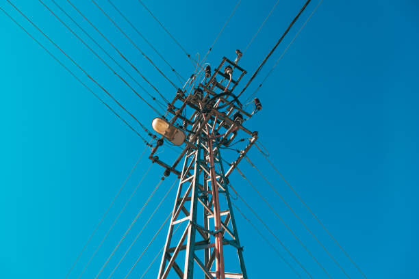 Electricity pole with overhead wires and street light lamp against blue sky