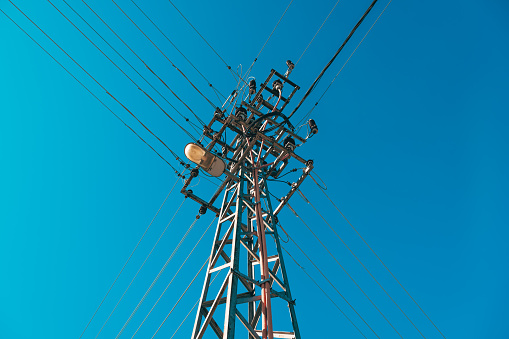 Electricity pole with overhead wires and street light lamp against blue sky