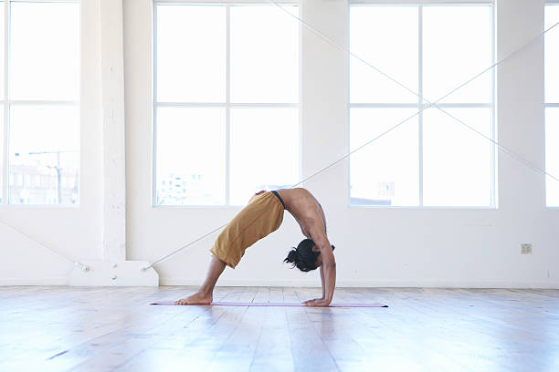 jeune homme pratiquant le yoga, performing posture du pont, vue latérale - yoga men bridge bending over backwards photos et images de collection