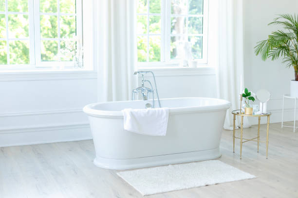 istock Stylish white bathtub against large windows and table with decoration. Concept of classic bath in modern apartment. Home decor ideas in contemporary bathroom scandinavian design. Template. Spa 2004681901