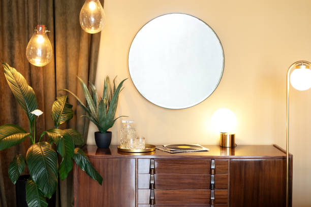 istock Dressing table with decorative elements in room. Mid century room in home with modern interior design, wooden cabinet, circular mirror, houseplants in pots and loft pendant lamps. Vintage cupboard 2004682422