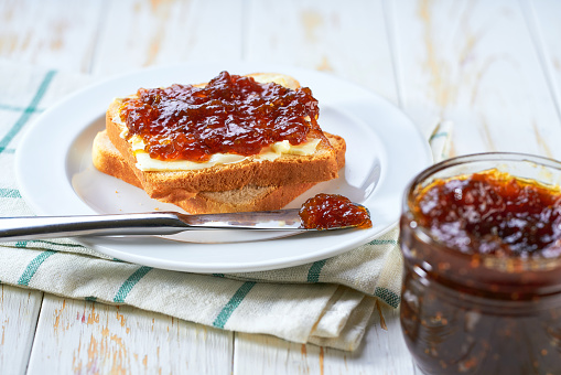 Plate with slices of bread and delicious figs jam on wooden table.