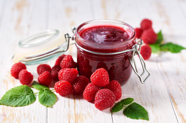 istock Glass jar of raspberry jam with fresh berries on a white wooden table. 2004686267