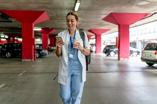 Pausing for a moment in a garage, a female nurse focuses on her phone to send an SMS, perhaps coordinating her next moves