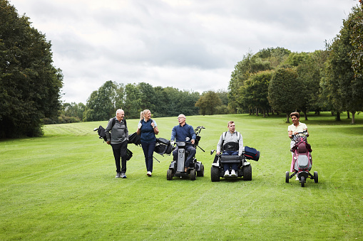 Sports, mobility scooter and people for golf game, match and competition on golfing course. Recreation, person with disability and women and men with caddy for training, fitness and practice outdoors