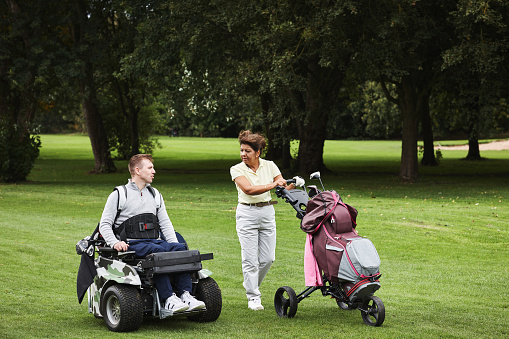 Sports, person with disability and people for golf game, match and competition on golfing course. Recreation, mobility scooter and woman and man with club for training, fitness and practice on field