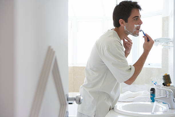 Man shaving face in bathroom mirror, side view  shaving stock pictures, royalty-free photos & images
