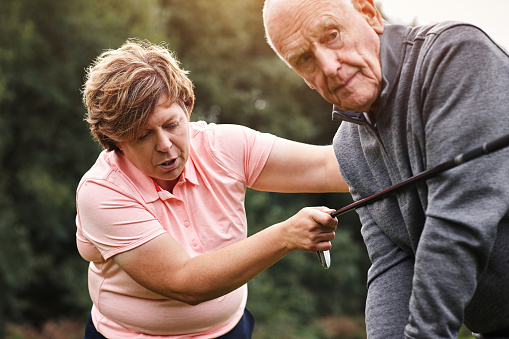 Golf course, coach and senior man learning at club, field or outdoor in nature to help at lesson. Golfers, instructor and teaching elderly person, exercise or training together for sports in summer