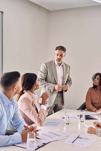 Busy senior company professional executive leader ceo manager leading business conference meeting managing consulting diverse corporate team workers at table in office board room. Vertical