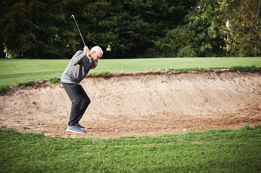 Golf, sand and man golfer playing with ball and metal club on outdoor pitch or field. Sports, mud and senior male athlete hitting equipment on outside course for match, training or game practice.