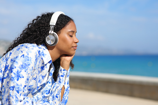 Black woman relaxing listening music with headphone on the beach