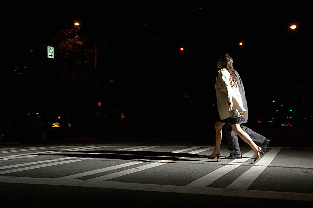 giovane uomo e donna di attraversare la strada di notte, vista laterale - walking at night foto e immagini stock