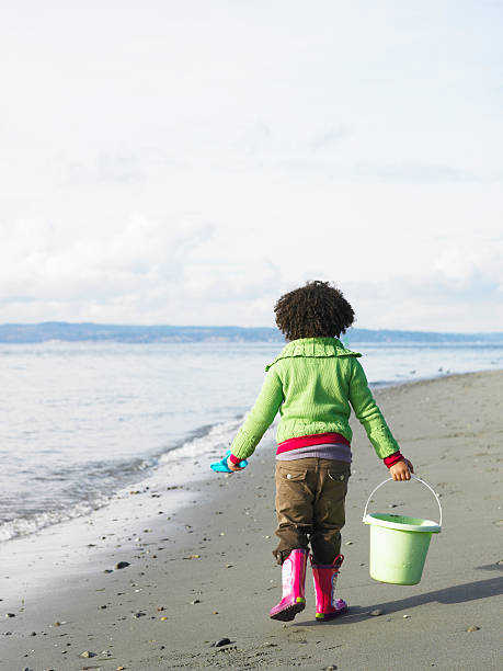 girl (5-7) transporte de cubo y pala en la playa, vista posterior - day washington state vertical outdoors fotografías e imágenes de stock