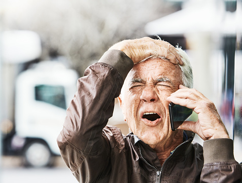 Startled man in his 70s gets bad news as he listens to his mobile phone outdoors in the city.
