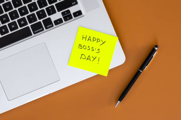 istock Sticky note with phrase Happy Boss Day attached to laptop on brown table. 2004835308