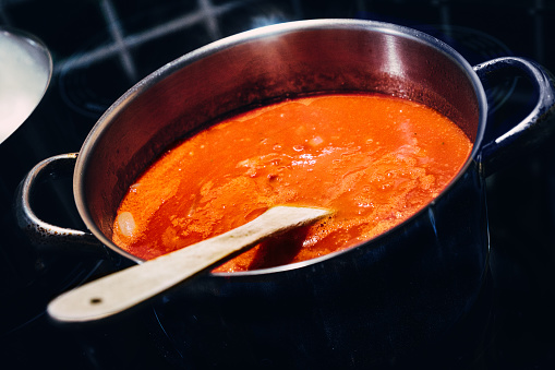 Mediterranean sauce with passata, onion, garlic and olive oil simmering in a stainless steel pan on the hob.