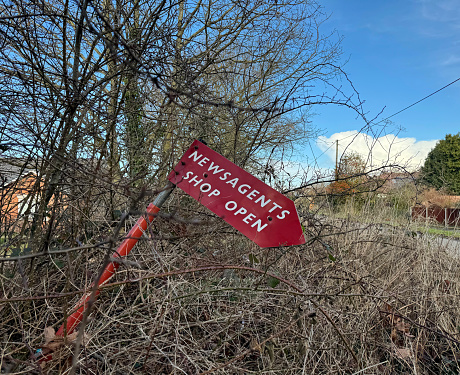 Directional sign in a hedge to a newsagents