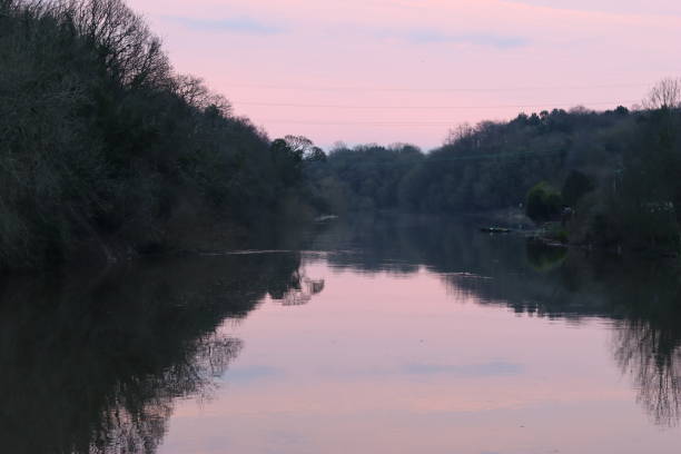view along a river at sunset, with a soft pink sky reflected in still water - color image light pink dramatic sky imagens e fotografias de stock