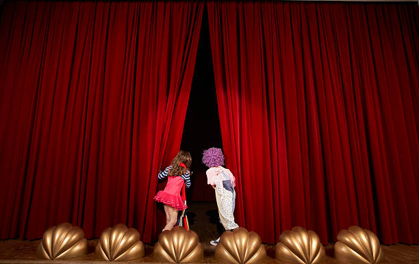 ragazza e ragazzo (5-7) sul palco, guardando attraverso tende - curtain red color image clown foto e immagini stock