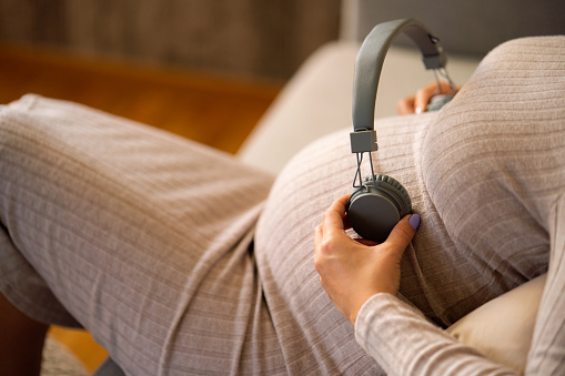 Close-up of unrecognizable pregnant woman with headphones on her stomach