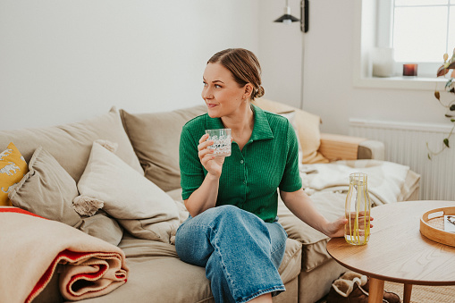 Woman indoors at home relaxing on sofa with glass of water