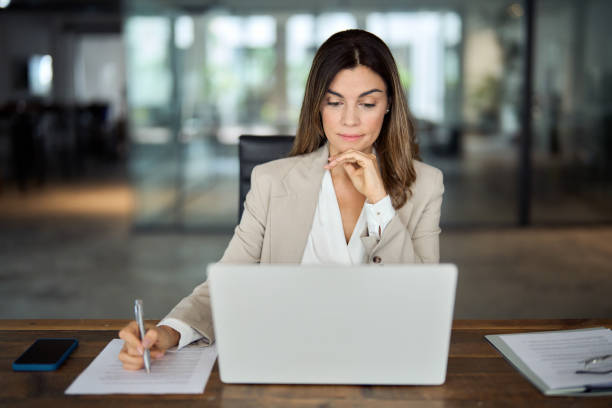 istock Busy mature business woman working in office using laptop writing notes. 2004890533