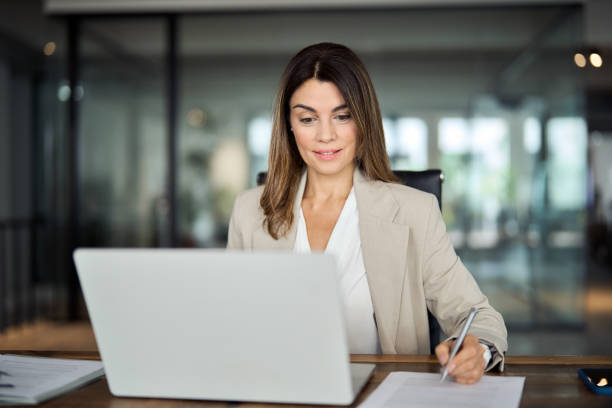 istock Busy mid aged business woman working in office using laptop writing notes. 2004890545