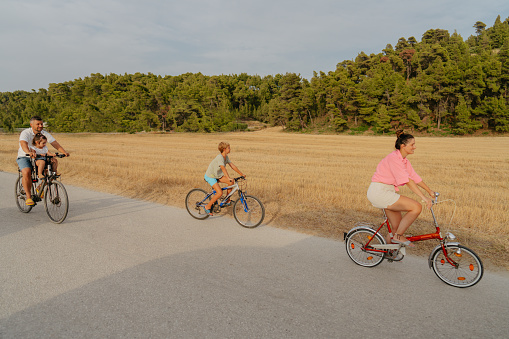 Photo of a young family, with two children, enjoy beautiful summer day riding bicycles by the sea