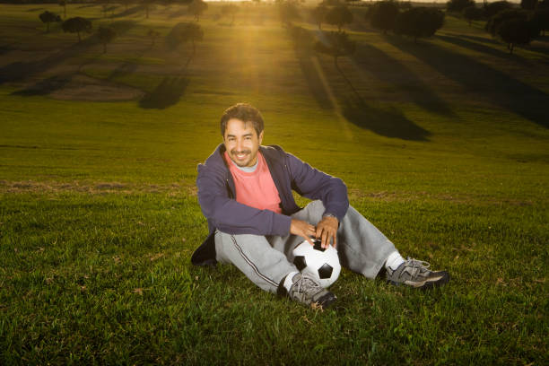 hombre sentado en el césped con pelota de fútbol - american football football focus on foreground team sport fotografías e imágenes de stock